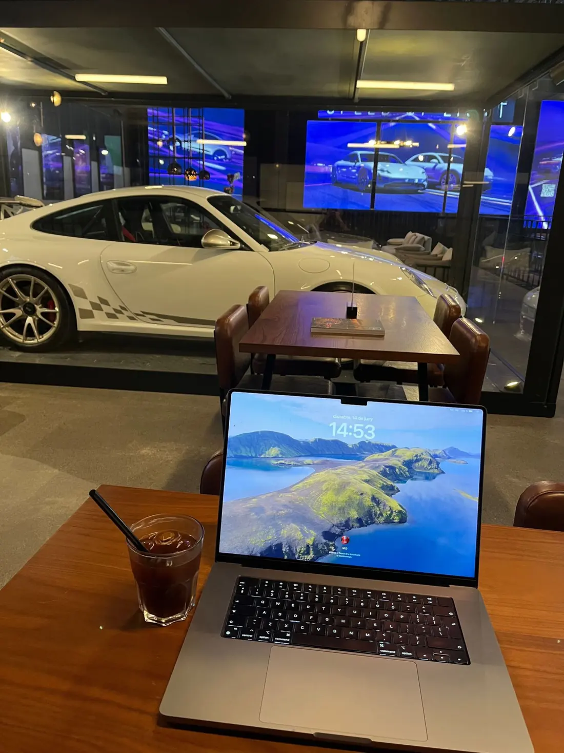 Marc Diez’s laptop and an iced coffee on a café table, with a white Porsche behind the glass